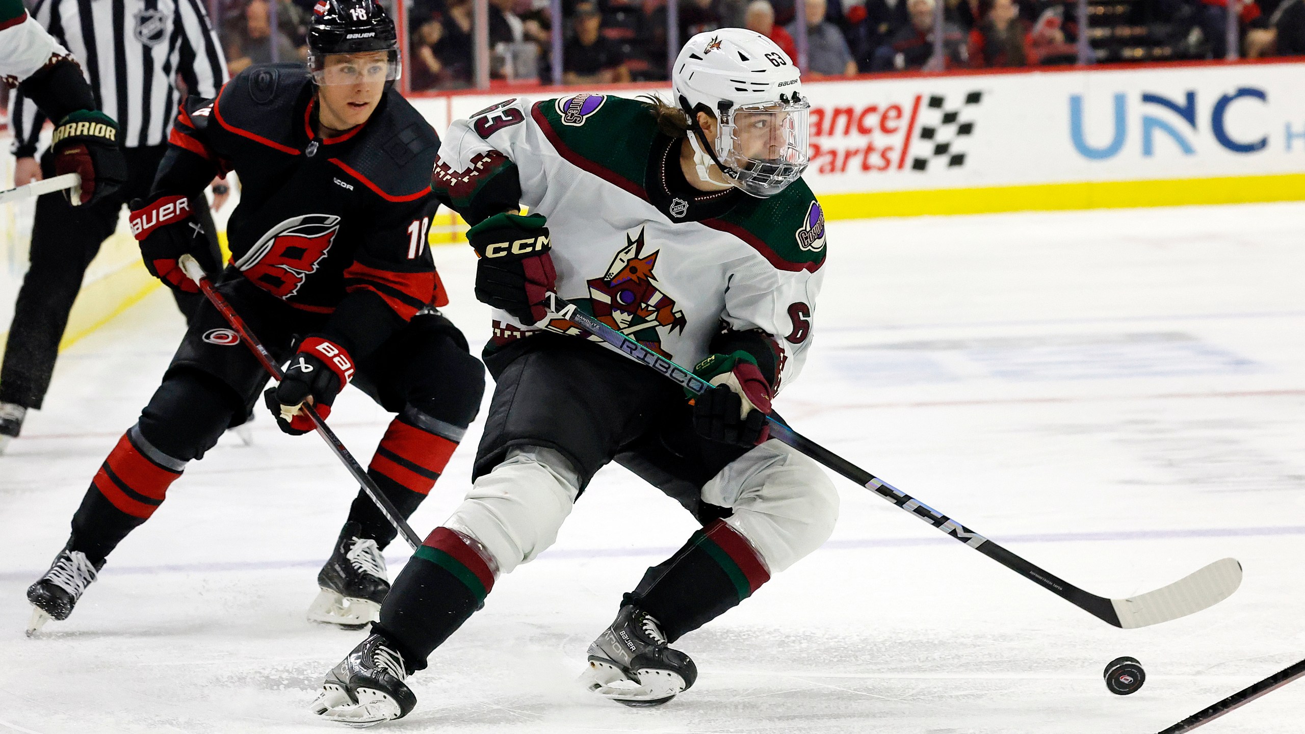 Arizona Coyotes' Adam Ruzicka (63) controls the puck in front of Carolina Hurricanes' Jack Drury (18) during the first period of an NHL hockey game Saturday, Jan. 27, 2024, in Raleigh, N.C. (AP Photo/Karl B DeBlaker)